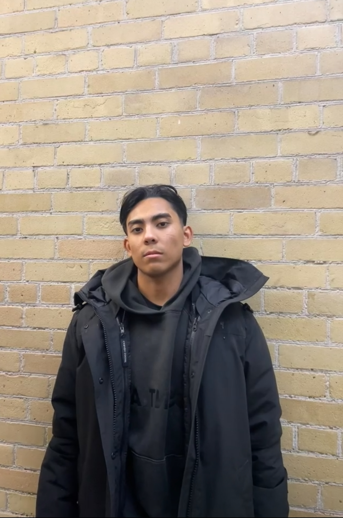 Daniel standing in front of a brick wall in a black coat.